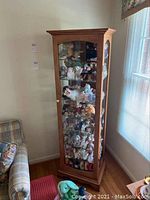 Front view of the wooden curio cabinet filled with various stuffed animals and toys, showing the glass door and wood detailing.