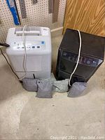Front view of white GE and black LG dehumidifiers with charcoal bags in front