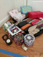 Lot of eyeglass cases, watches in decorative boxes, jewelry boxes in floral and patterned designs, and a small folding clock on wooden floor.