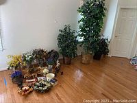 Wide view of hardwood floor corner showing three faux trees in baskets at back and floral items at front
