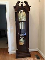 Full front view of the wooden case, hood, weights, pendulum and base
