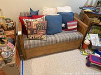 Full front view of the wooden love seat with blue plaid cushions and multiple decorative pillows including star and patchwork designs.