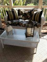 Whole set showing the loveseat with floral cushions, the glass top coffee table, and two candle lanterns on the table