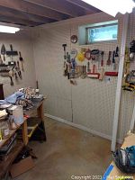 Wide shot of basement workshop pegboard with various painting brushes, rollers, and tools hanging for sale.