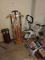 Photo showing the Speedway sled, a wooden sled with metal frame and a white Ergometer exercise bike along with boxes containing manuals or books.