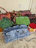 Multiple Vera Bradley floral and paisley patterned handbags with Scout duffle bag and cosmetic pouches on floor
