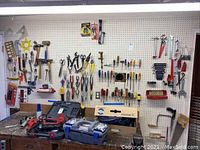 Wide view of pegboard with various hand tools hanging and workbench with cases and boxes containing more tools.