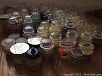 Overhead view of approximately 30 glass jar candles arranged on wooden floor showing assorted sizes and colors