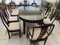 Oval glass-top table with six chairs arranged around, viewed front-on.