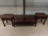 Set of three rosewood accent tables in front of window blinds on tiled floor showing overall table shapes and arrangement.