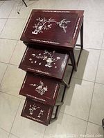 Photo showing all 4 rosewood nesting tables stacked inside each other from top angle, highlighting the inlaid white floral and vine designs on each table surface and the reddish-brown finish.