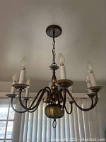 Front and side views of bronze plated six-light chandelier with electric candle bulbs installed, hanging from ceiling mount with chain.