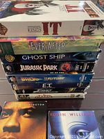Stacked view of VHS movies including IT, Ever After, Ghost Ship, Jurassic Park, Back to the Future, E.T., and others.