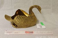 Side view of brass swan planter with measuring ruler showing length.
