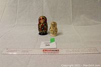 Shows two sets of nesting dolls next to a ruler for scale, with the red set taller than the beige set.