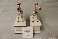 Front view of two white ceramic zebra figurines with brown stripes, standing on matching pedestals.