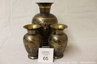 Three black metal vases with gold floral design and detailing displayed against a white background.