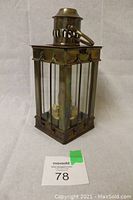 Front angled view of the vintage British metal lantern showing its rectangular shape, vertical glass panels, metal frame, and vented top with carrying ring.