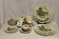 Full view of teacups, saucers, and plates arranged with some plates on display stands, showing the painted small town design.