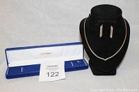 Full view of the matching silver necklace and earrings displayed on a black necklace bust and in a blue Dynasty box, showing set details and presentation box.