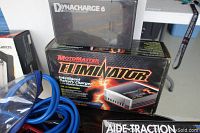 Boxed MotoMaster Eliminator Intelligent Battery Charger with lightning design on packaging, placed beside blue charging cables and a Dynacharge 6 charger with a transparent cover.