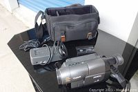 Canon ES300V camcorder, charger, and carrying case displayed on black glass surface.