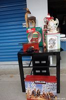 View of all Christmas items on black table including jewelry music box, deer figurine, Santa chair figurine, snow globe, and Kirkland nativity box.