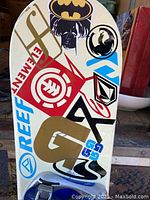 Photo of snowboard top showing multiple colorful stickers and bindings attached, with signs of wear.