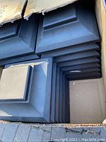 Box of square black fence post caps stacked inside with stepped design visible