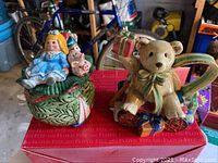 Photo of two Fitz and Floyd Christmas figurines showing the girl with pig on a green leaf-patterned base and teddy bear holding gifts on a holly-decorated base.