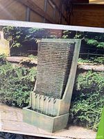 Photo of the outdoor wall fountain in an outdoor garden setting showing its textured front and water basin.