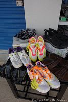 Photo showing multiple pairs of shoes including Saucony neon yellow and pink running shoes, white and orange laced shoes, black and gray Brooks shoes, white and purple Brooks shoes, and brown Rockport sandals.