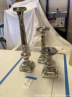 Three mercury glass pillar candle holders arranged on table with white cloth background showing full height and base shape