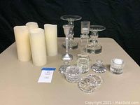 Lot showing flameless pillar candles, glass Lucite candle holders, silver metal candlestick, and crystal votive holders arranged on a table.