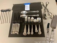 Full flatware and serving utensils set neatly organized on black fabric background showing all pieces.