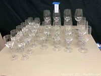 Full set of 28 clear glass wine and goblet glasses arranged on table under lighting