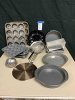 Full set of bakeware items arranged on table including muffin tins, Bundt pan, springform pan, loaf pans, sifter, and cake boards