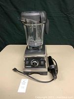 Front view of blender base with container, lid and tamper laid on table