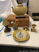 Whole lot showing wicker basket, brass urn, painted plate, blue and yellow pitcher, boudoir lamp, and brass candle holder