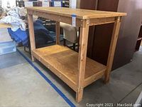 Full view of the handmade tall wooden workbench in natural wood finish showing top surface and lower shelf with sturdy wooden legs and metal fastenings.