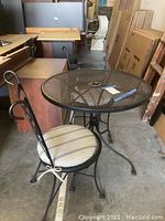 Overall view of wrought iron patio set including round mesh table and 2 chairs with cushions in storage setting
