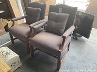 Pair of upholstered arm chairs in faded slubbed fabric with matching pillows, wooden arms and legs with visible wear.