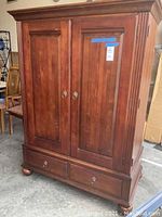 Full view of the brown wooden TV armoire showing double doors and bottom drawers