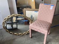 Pink brocade upholstered side chair, oval mirror with twisted gold distressed frame, and framed floral print artwork leaning against the wall.