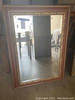 Full view of the rectangular mirror leaning against a dark surface, showing the wood frame with gold ornamental trim.