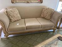 Front view of beige fabric sofa with carved wooden frame and two paisley decorative pillows.