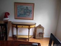 Photo showing full view of half-moon table, framed artwork hanging on wall, and ornate mirror leaning against wall