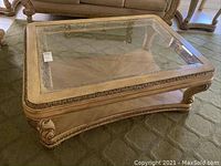 Front view of rectangular glass top coffee table with carved wood frame and lower shelf.