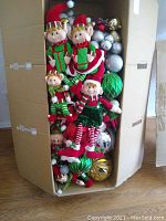 Box filled with plush elves and assorted ornaments visible behind them