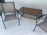 Glass top patio coffee table alongside two metal frame mesh chairs, showing the weathered condition and matching design.
